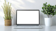 © siraphol - White laptop mockup centered on desk with potted plants creating calm workspace scene