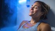 © mila103 - A woman with a content smile sits in a cryotherapy chamber experiencing cold therapy after exercise. The blue light enhances the relaxing atmosphere promoting recovery and wellness.