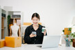 © Nuttapong punna - Startup small business SME, Entrepreneur owner woman using smartphone or tablet taking receive and checking online purchase shopping order to preparing pack product box.