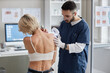 © Seventyfour - Caucasian woman sitting while male dermatologist examining skin on back using magnifying glass during medical consultation in clinic, patient turning slightly to show affected area