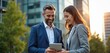 © Maryna - Man and woman in suits smile while looking at tablet outside modern office building. Business partners discuss project details, happy about good results and future plans.