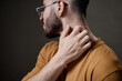 © Seventyfour - Young adult man scratching neck with right hand, showing discomfort, side profile visible, short beard and glasses, neutral background