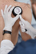© Seventyfour - Caucasian middle aged man undergoing skin examination by male dermatologist using dermatoscope on back, dermatologist wearing gloves and carefully inspecting moles for signs of skin conditions