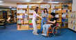 © Raushan_films - Indian young adult male man sitting wheel chair use tablet take part group study speak show screen share new ideas indoor gen z pupil teen girl boy hold book talk library college place