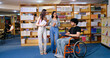 © Raushan_films - Indian young adult male man sitting wheel chair use tablet take part group study speak show screen share new ideas indoor gen z pupil teen girl boy hold book talk library college place