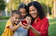 © Vadym - Smiling mother shares phone content with laughing kids in park. Family bonding, joy, and shared digital moments outdoor. Parent and children enjoying screen time.