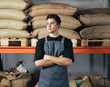 © Artem Varnitsin - Confident barista standing at warehouse with arms crossed. Male worker in apron standing against shelf with bags at warehouse.