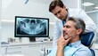 © Nikolay_md - An adult patient holds his jaw in pain while the dentist analyzes a digital X-ray of his teeth to diagnose the problem.