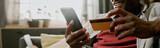 Website banner of Black man holding smartphone and credit card making online purchase sitting indoors smiling, focusing on screen