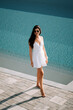 © Darius - Woman in white dress walks by resort pool on sunny day