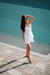 © Darius - Woman in a white dress walking by a poolside on a sunny day