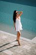 © Darius - Woman walking gracefully by a clear pool in a summery white dress during sunny daylight