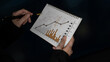 © InfiniteFlow - A close-up view of hands holding a notepad filled with graphs and charts, illustrating data trends for business analysis and financial planning in a professional setting. Scalp