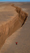 © AmazingAerialAgency - Aerial view of a dramatic chasm cleaves through the ochre earth, a lone figure stands silhouetted against the stark beauty of the arid landscape, Shahdad, Kerman Province, Iran.