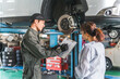 © buritora - A female customer and a male mechanic receive an explanation about a car that has been lifted for a vehicle inspection