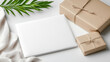 © siraphol - White parcel mailer mockup on minimalist table with wrapped kraft gifts and green leaf