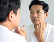 © baeeo - Middle-aged Asian man looking at reflection in the mirror, touching his face