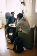 © Maskot - Rear view of curly haired teenage boy leaning on elbow while sitting with counselor in high school office