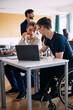 © Maskot - Physically disabled student studying on laptop with male classmate in classroom at high school