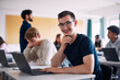 © Maskot - Portrait of physically disabled happy young man sitting with hand on chin at desk in high school classroom