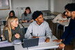 © Maskot - High angle view of male teacher assisting teenage students sitting at desk in classroom at school