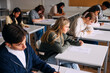 © Maskot - High angle view of male and female students giving exam while sitting at desk in classroom