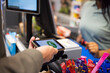 © Maskot - Hand of man using tap to pay method through smart phone at supermarket checkout counter
