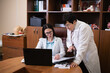 © Oleksandr Maliev - Two female doctors wearing white coats working together, discussing patient data and research findings on a laptop and documents in a healthcare office setting