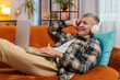 © Andrii Iemelianenko - Happy relaxed Caucasian young man with gray hair in wireless headphones lying on home couch sofa choosing listening disco music while working on laptop netbook. Guy weekends activities entertaining