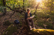 © Maskot - High angle view of woman reading book while sitting on tree trunk in forest