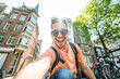© Davide Angelini - Happy tourist taking selfie picture in Amsterdam, Netherlands - Cheerful man using smart mobile phone device outside - Student traveler enjoying summer european vacation - Life style tourism concept