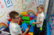 © Maryia - Two brothers building with giant colorful blocks in play zone at indoor playground with doodle wall behind. Concept of siblings creative play, construction fun and educational kids entertainment.