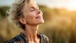 © Babb - A woman stands in a sunny field with her eyes closed savoring the warm breeze and tranquility of the sunset. Her relaxed smile reflects pure contentment and joy in the moment.
