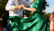© Anna - A couple in traditional costumes performing a folk dance outdoors. Close-up on holding hands and the motion of a swirling green satin dress during a cultural festival.