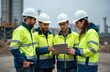 © miss irine - Team of experts in safety wear works at construction. Men and woman watch the tablet and discuss plan. Engineers inspect industrial object outdoor. Safety control and management.