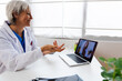 © Xavier Lorenzo - Mature adult doctor talking with female colleague through video call sitting on desk at medical consultation. E-learning, business and healthcare education concept
