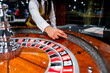 © Productions - Croupier launching roulette ball on glossy casino wheel, highlighting gambling, betting strategy, risk, luck and entertainment.