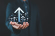 © Nirusmee - Businessman holding a virtual glowing upward arrow, symbolizing business growth, strong financial performance, investment success, and a positive economic trend with percentage icons.