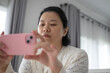 © Kwangmoozaa - Focused Asian woman holding a pink smartphone horizontally to take a photograph or record a video indoors in a modern home environment