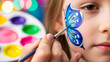 © Lexi - Girl getting butterfly face paint applied with colorful palette in background