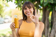 © luismolinero - Young woman holding an orange juice at outdoors showing ok sign with fingers