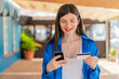 © luismolinero - Young pretty woman at outdoors buying with the mobile with a credit card