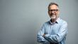 © Vadym - Smiling mature man poses in studio. Grey hair person in eyeglasses with beard looks at camera. Male wears blue shirt, crossed arm gesture. Positive human face expression in confidence.
