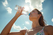 © Vadym - Young woman drinks water from bottle. She hydrates under bright sunny blue sky. Female refreshes body outdoors in hot weather. Healthy girl enjoys clean pure beverage. This person stays active.