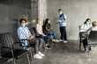 © Prostock-studio - Multiethnic people different ages sitting at clinic hall, wearing medical face masks, waiting for immunization against COVID-19 while pandemic, male doctor having conversation with patients