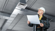 © Grispb - HVAC installation specialist reviews ventilation schematics while inspecting air ducts, ensuring correct system layout and proper airflow setup in a commercial building.