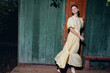 © SHOTPRIME STUDIO - Portrait of a woman model in a flowing yellow dress stands by a weathered doorway in an outdoor night setting, striking a poised pose and glancing back, exuding elegant fashion and moody cinematic