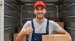 © Vasiliy - A smiling delivery man holding a cardboard box shows a thumbs up. A professional mover in uniform stands inside a moving truck. Relocation and logistics service concept