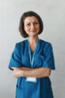 © shurkin_son - Vertical portrait of mature female healthcare worker posing with crossed hands and looking at camera with smile, dressed in blue uniform, advising to get check-up in her clinic, isolated on gray