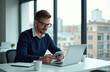 © Viktor - Man works at office using tablet and laptop. He wears glasses. Office setting with natural light and city view. Businessperson focused on work. Modern workplace. Coffee cup on desk.